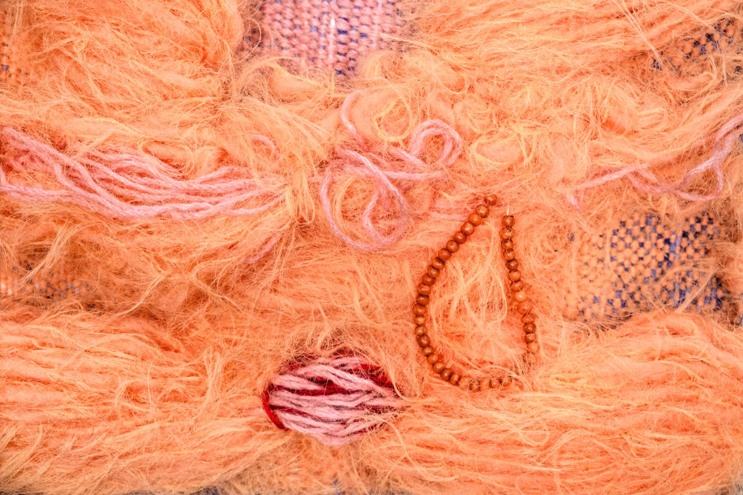 Detail of Abundance: close-up of apricot mohair and pink threads around a teardrop of wooden beads and a wrapped pink and red knot