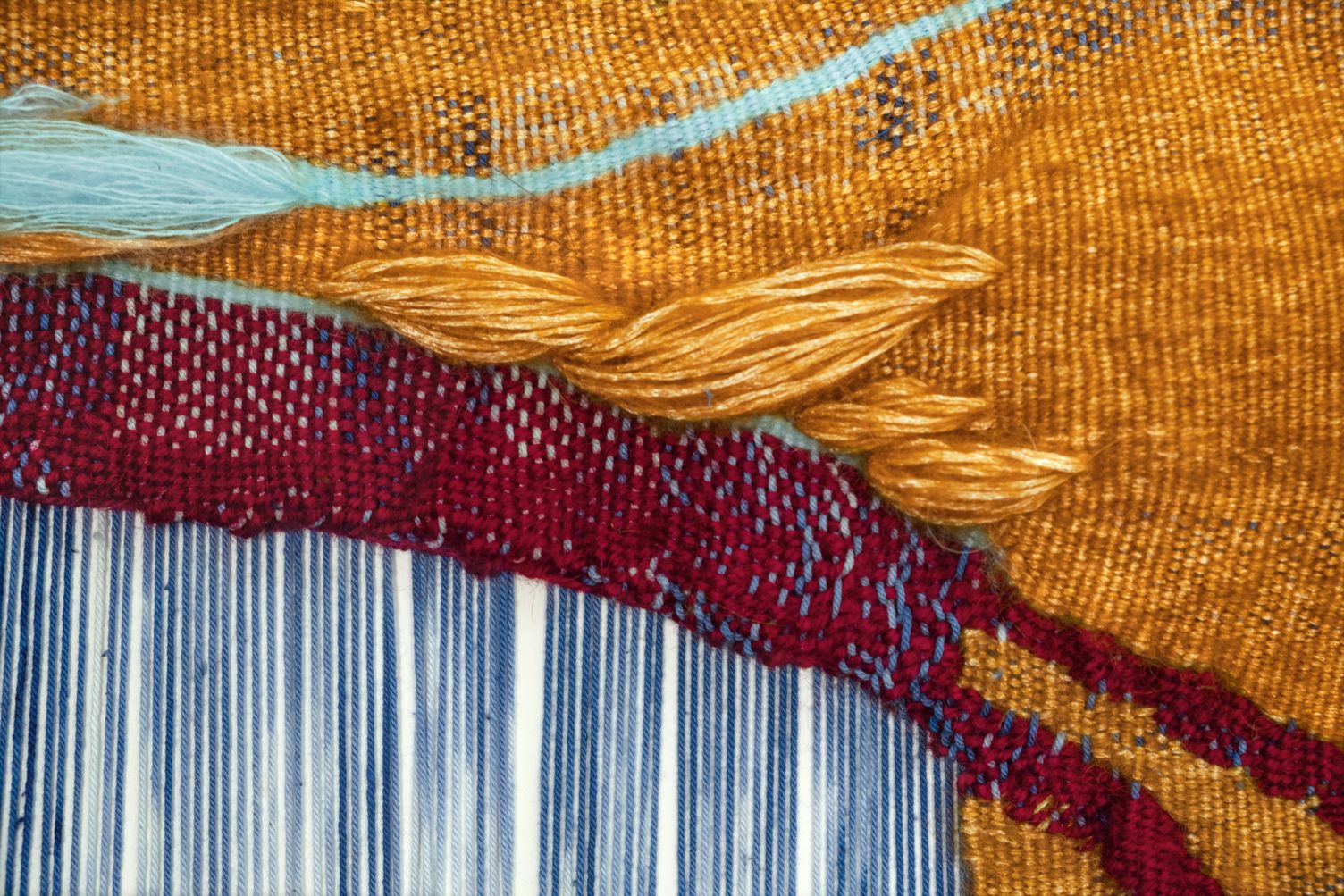 Detail of All For Us to Enjoy: close-up of the golden twisted strand and a turquoise thread on ochre, edging a wine red band over blue warp