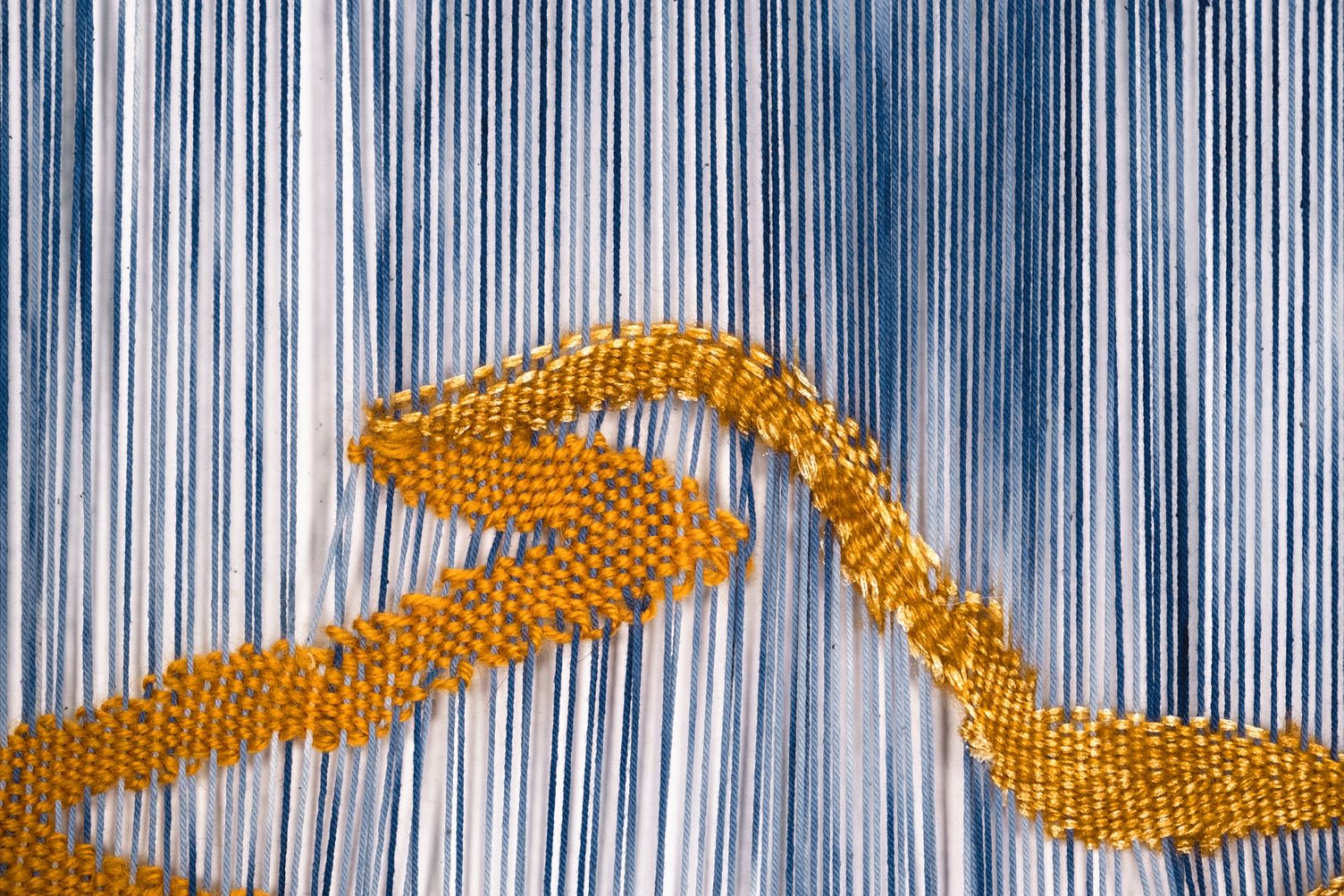 Detail of It is a Journey: close-up of the ochre woven path, its threads catching the light against the dense blue and white warp