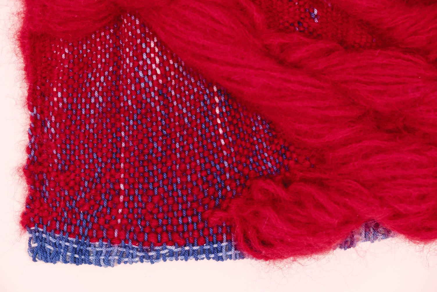 Detail of Love: the lower corner, red mohair spilling over a red and blue woven ground with a blue edge