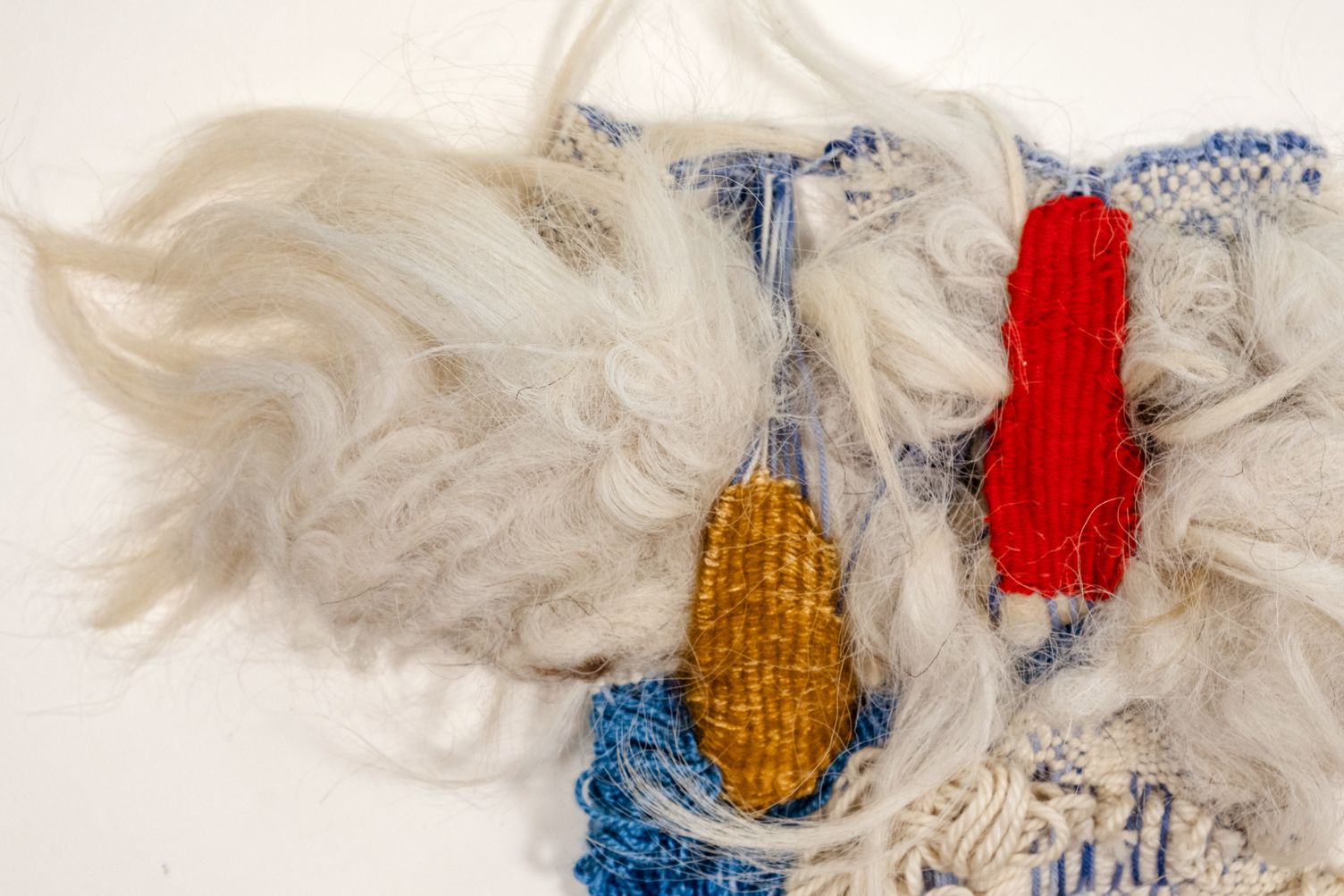 Detail of Peace: white curly wool around a red and an ochre woven shape, above blue weaving