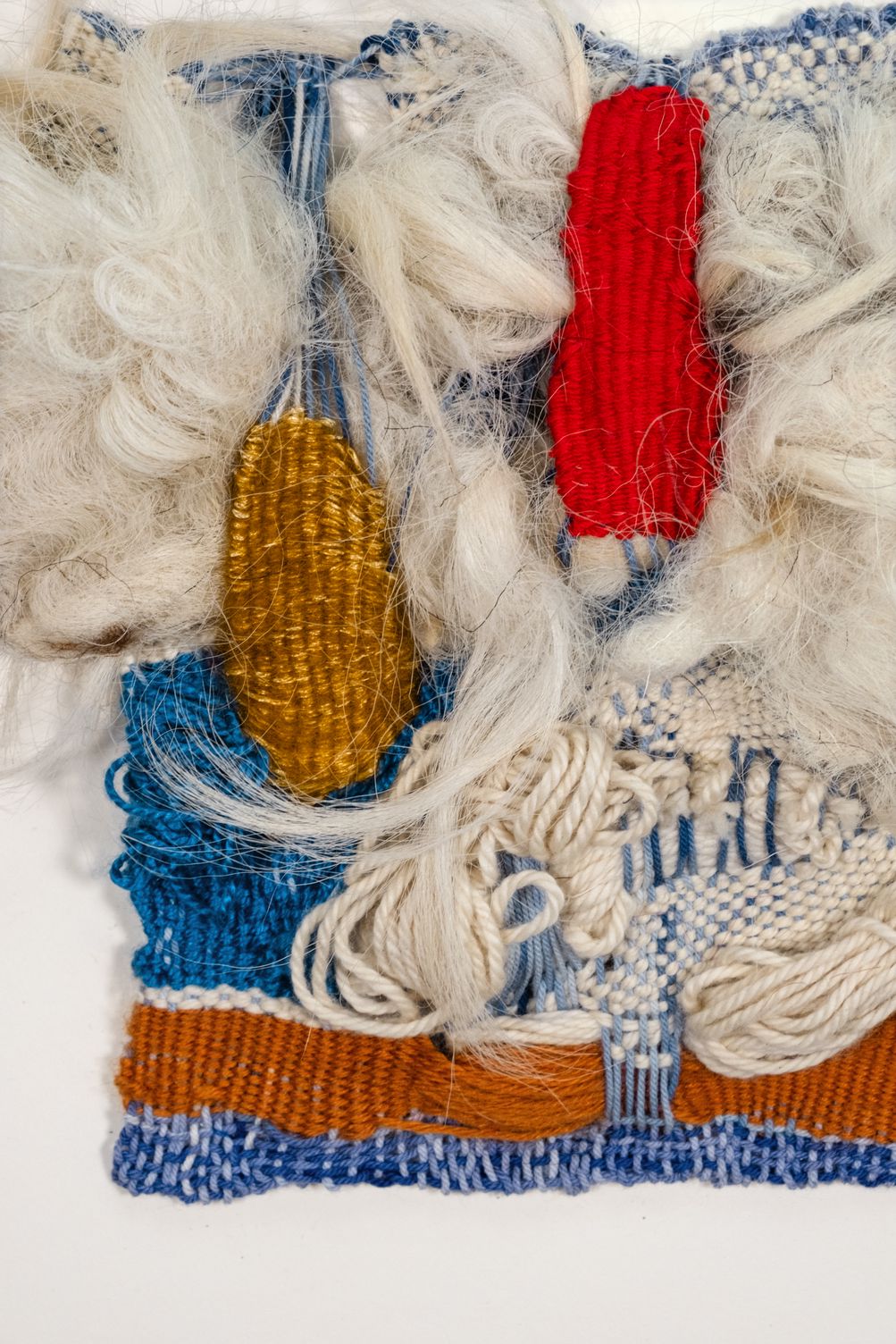 Detail of Peace: a red and an ochre woven shape among white curly wool, above blue, cream and rust bands