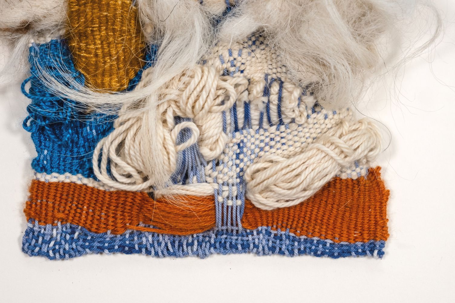 Detail of Peace: cream yarn loops and blue weaving above a rust band and a blue lower edge