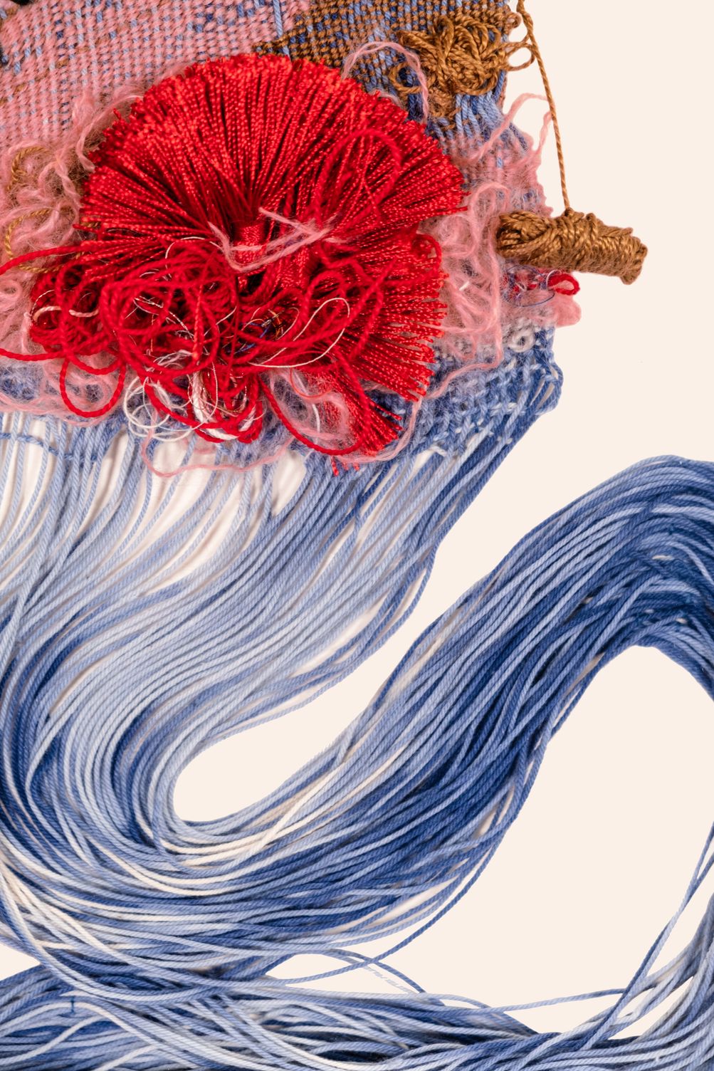 Detail of The Air is Fragrant: a red tassel and loops of red thread over pink mohair, an ochre wrapped knot, and loose blue cotton warp threads sweeping down in a wave
