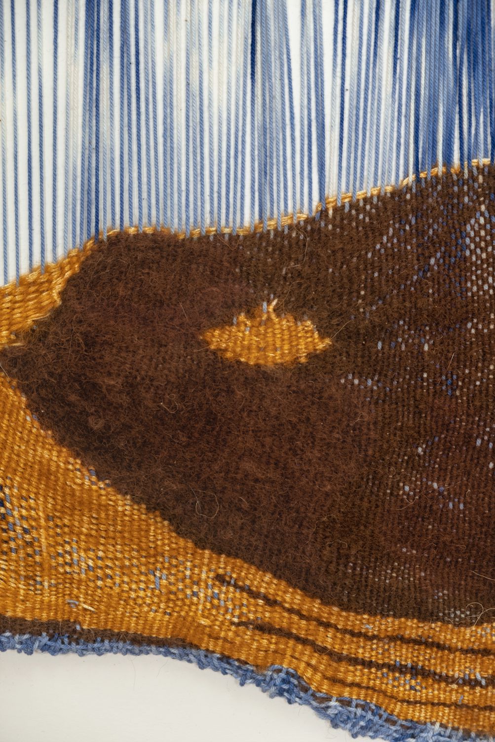 Detail of The Temperature Sweet: a dark brown mohair hill with a small ochre opening, against ochre weaving and open blue and white warp