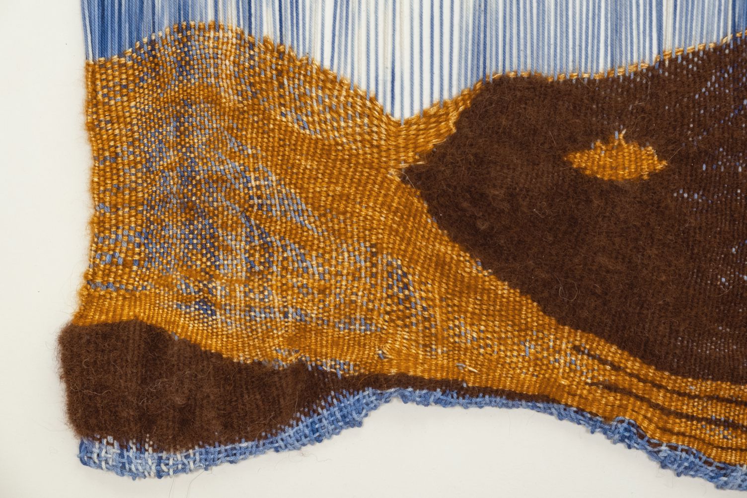 Detail of The Temperature Sweet: an ochre and dark brown mohair landscape with traces of blue, its lower edge finished in blue