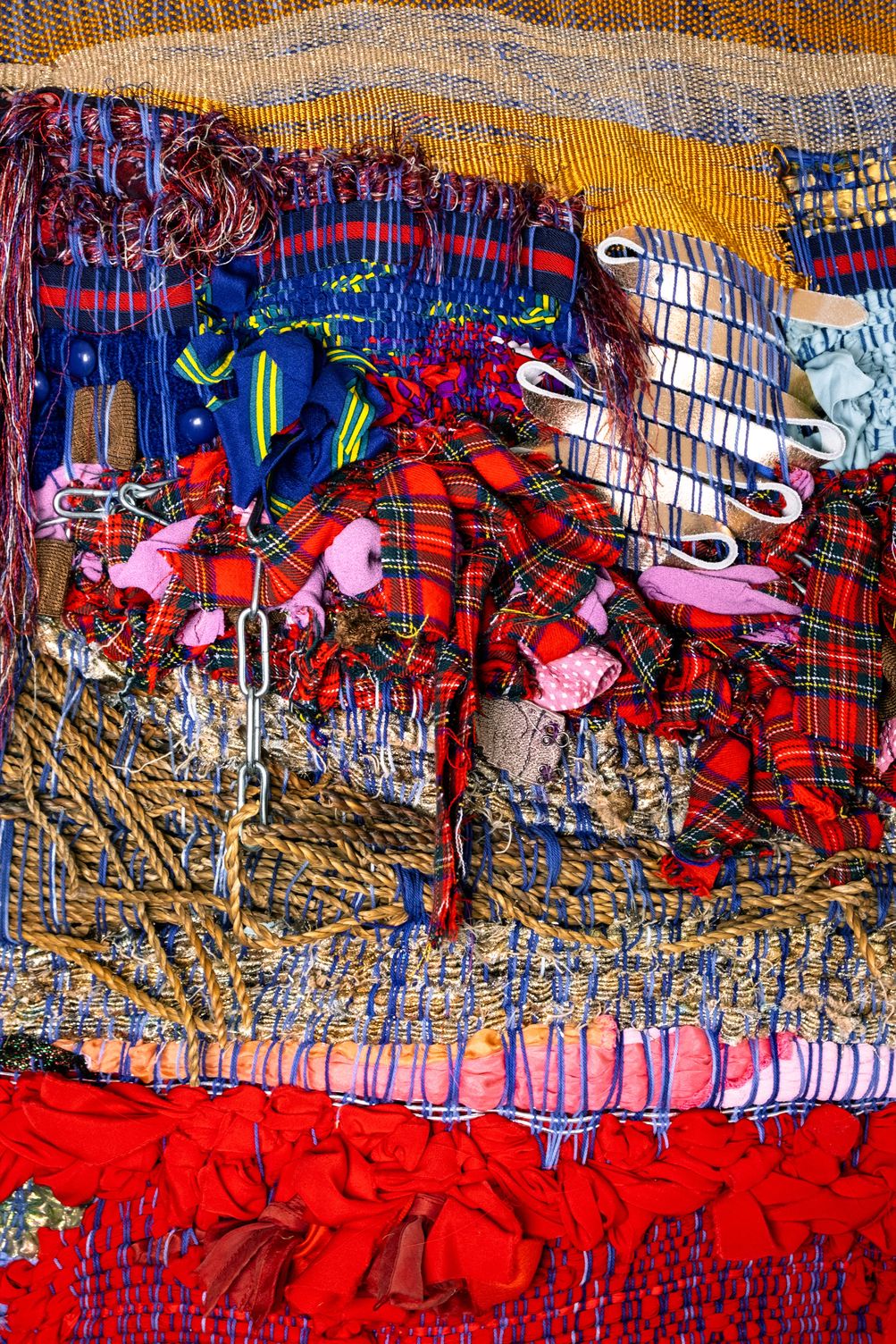 Detail of Freedom: red tartan scraps, a metal chain and pieces of a wicker chair woven into blue and gold warp, above rope and red fabric