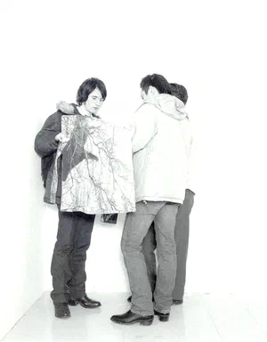 All Events Are Even, page 3: black-and-white photograph of three young men, backs to the camera, one holding up a garment printed with bare branches