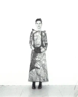 All Events Are Even, page 4: black-and-white photograph of a woman standing alone in a full-length branch-print dress, hands clasped at her waist