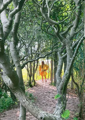 Numéro Homme Berlin, Volume C-18, Spring/Summer 2024, page 20: full-page fashion photograph, a figure in an orange tunic and shorts on a wooded path, vertical credit naming a Claudia Hill dress